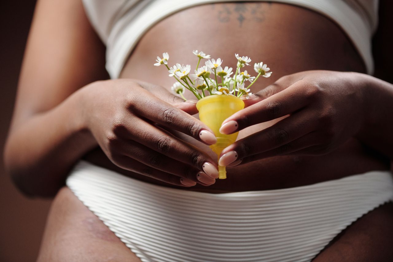 about-02 Close-up of a woman's hands holding a menstrual cup filled with flowers, symbolizing femininity and care.