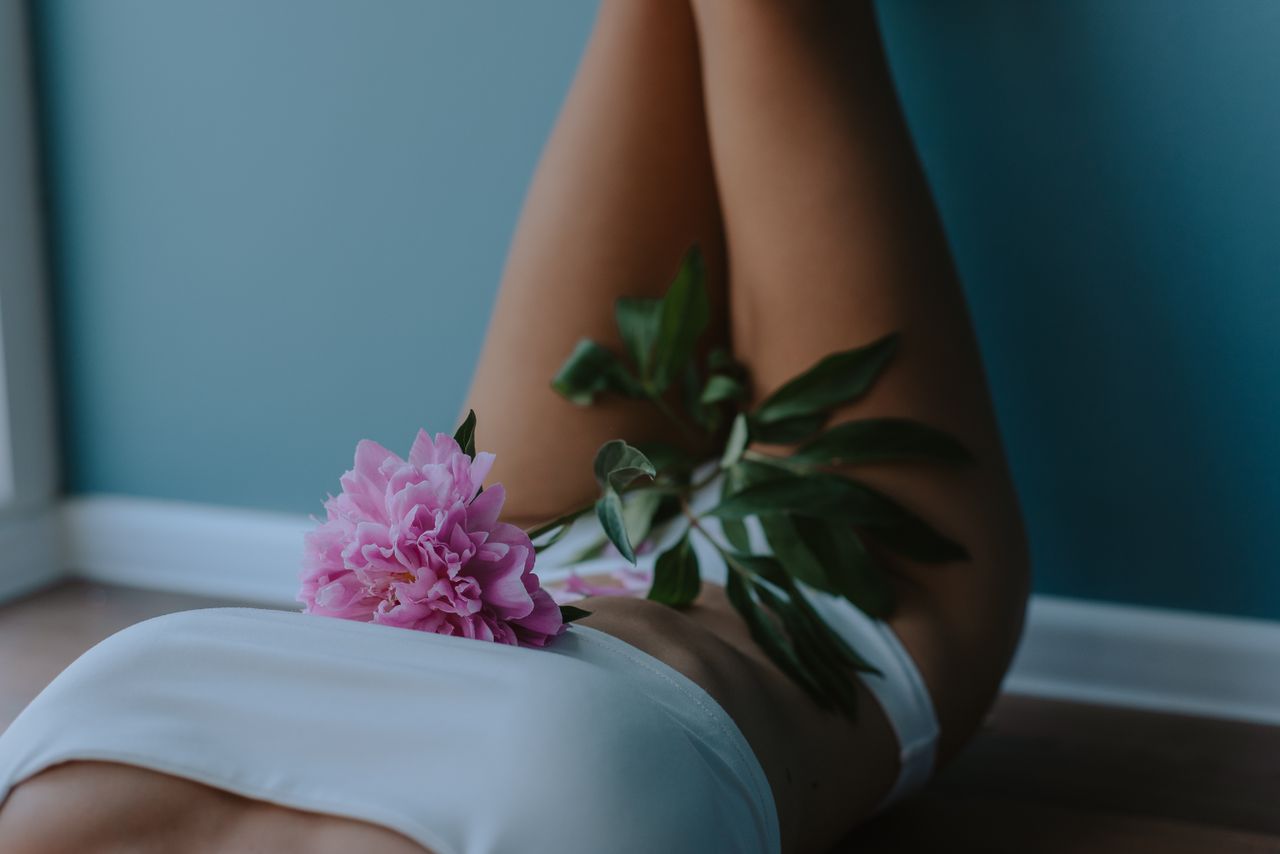 ours-journey Woman relaxing indoors with pink peony flower on her body, embodying tranquility and self-care.